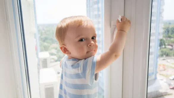 Ein Kleinkind öffnet ein Fenster in einem Plattenbau von innen