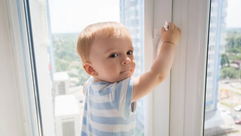 Ein Kleinkind öffnet ein Fenster in einem Plattenbau von innen